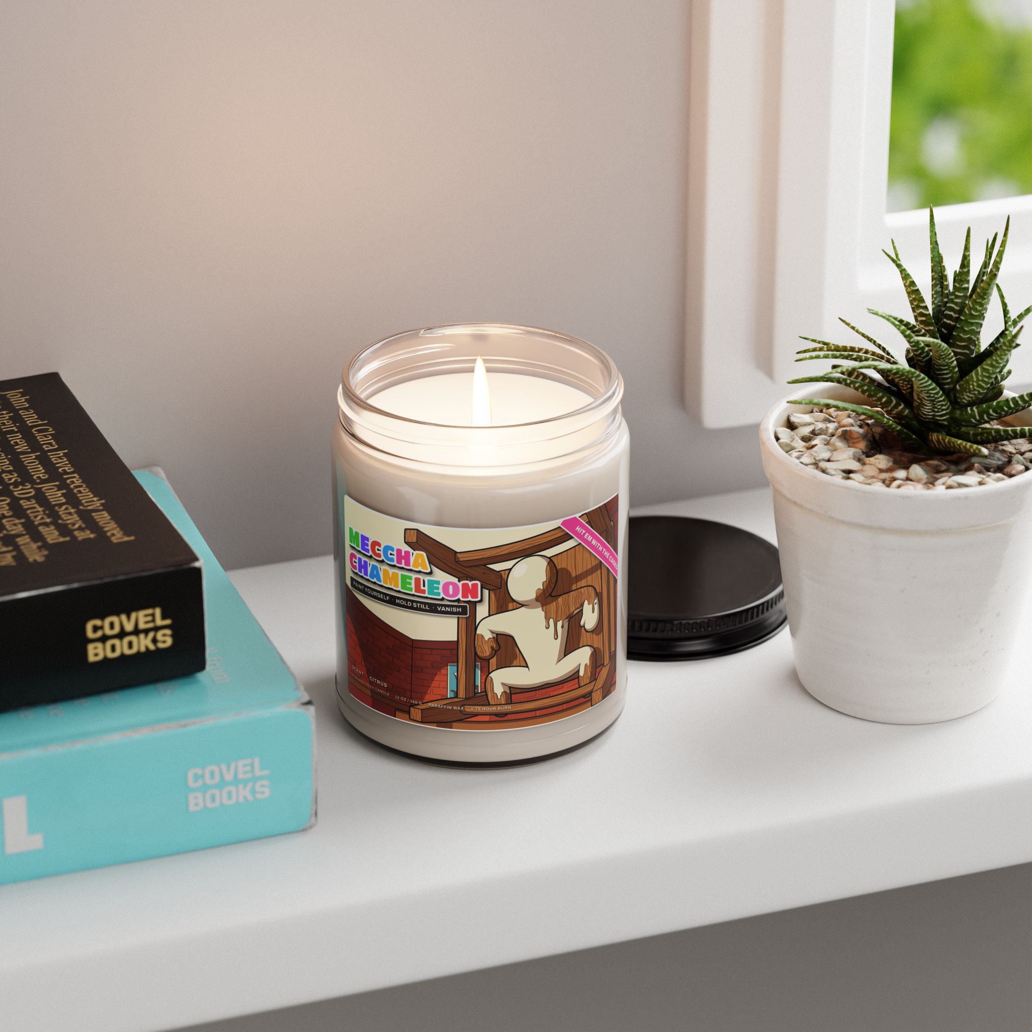 Meccha Chameleon candle lit on a bright windowsill next to books and a small plant